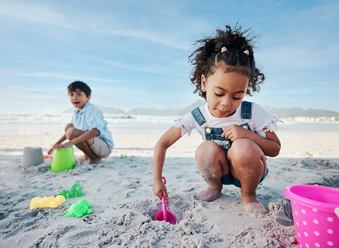 Boy, girl and shovel with bucket, beach and digging sand with playing, outdoor and vacation in summer. Kids, siblings and plastic toys for sandcastle, construction game and happy for holiday by ocean