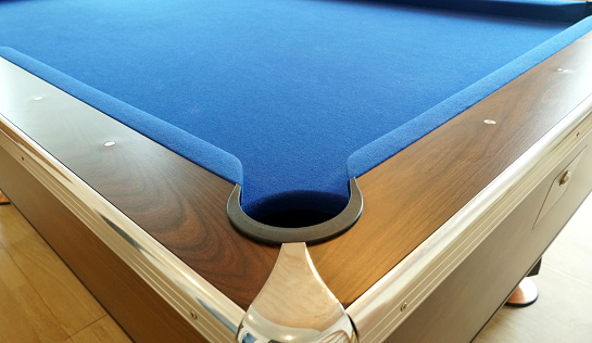 A hole in the corner of a pool table with a wooden border. and covered with a blue flannel cloth.