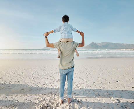 Dad, child on beach and piggy back together in summer waves on tropical island holiday in Hawaii. Fun, father and son on ocean vacation with love, support and relax at water with blue sky from back.