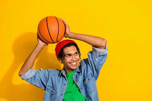 Photo portrait of attractive young man hold basketball ball look empty space wear trendy jeans clothes isolated on yellow color background.