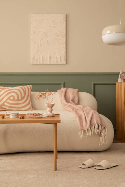 istock Warm and cozy living room interior with mock up poster frame, wooden coffee table, patterned pillow, pink plaid, white slippers, beige rug and personal accessories. Home decor. Template. 1753964712