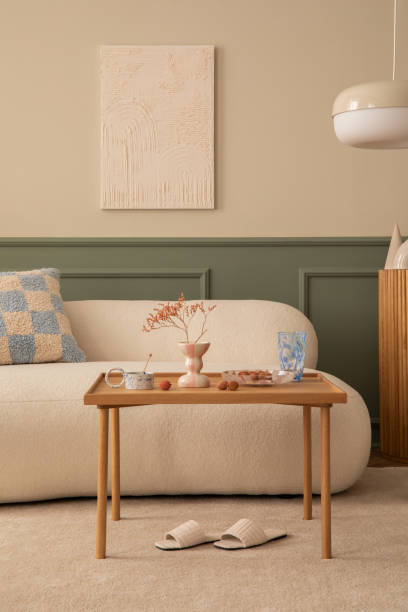 istock Warm and cozy living room interior with mock up poster frame, wooden coffee table, patterned pillow, pink plaid, white slippers, beige rug and personal accessories. Home decor. Template. 1753965334