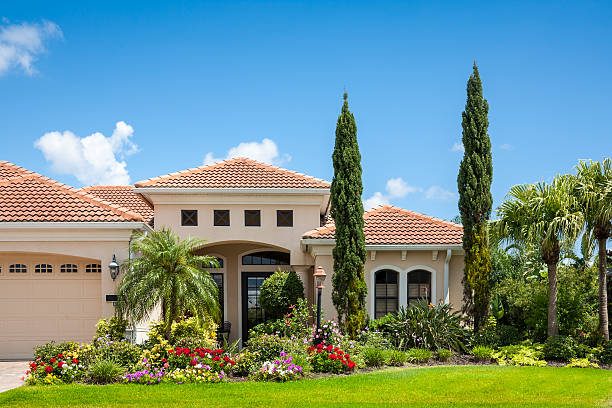 Home with Flower Garden "New upscale home with flower garden, palm trees, cypress trees and lush tropical foliage. Front yard; clear blue sky." ornamental garden palm tree bush flower stock pictures, royalty-free photos & images