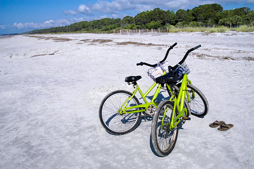 Two bicycles and a pair of flip flops are parked on an empty beach on Hilton Head Island, South Carolina. Space for copy on left side of image.