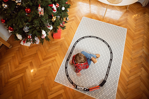 Little boy sitting on the floor at home and playing with his Christmas gift.