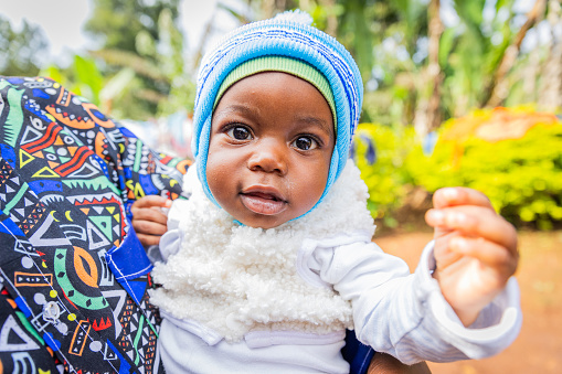 Cute healthy little African baby boy carried in an adult's arm looking at the camera.