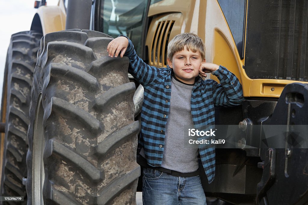 Boy standing in front of tractor Boy (8 years) standing by tractor wheel. Boys Stock Photo