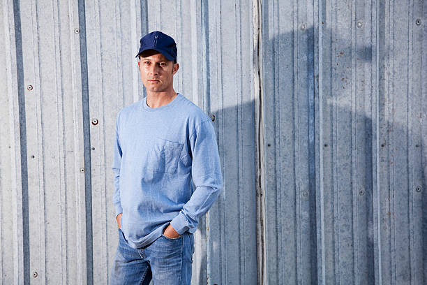 Serious man in cap standing outdoors Serious man (40s) wearing baseball cap and jeans three quarter length photos stock pictures, royalty-free photos & images