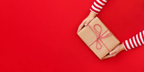 istock Christmas banner gift box in children's hands on a red background, presenting a gift 1753969875