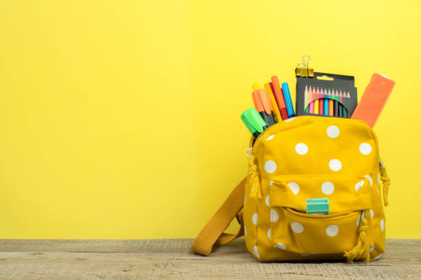 istock Yellow backpack with white polka dots with different colorful stationery on table. Yellow background. Back to school. 1753970415