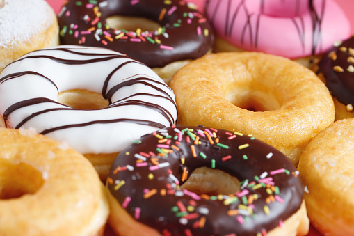 assorted donuts with chocolate frosting, topping sprinkles donuts Colorful variety and Variety of flavors mix of multi colored sweet donuts with frosted sprinkled on pink background. top view