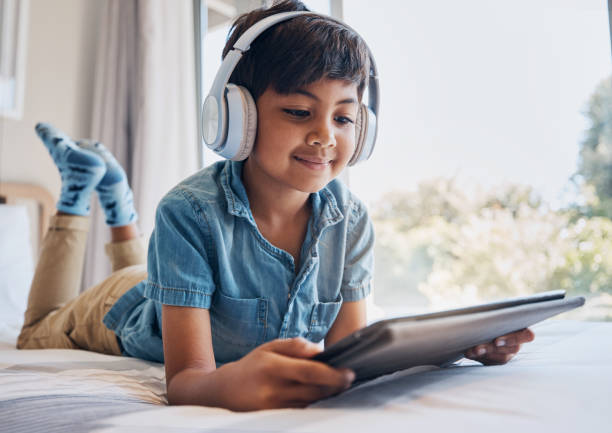 ragazzo, tablet e cuffie a letto, lettura del sorriso per l'abbonamento in streaming, film o relax con video. bambino maschio, touchscreen digitale e pensiero in camera da letto per audio, spettacolo o elearning a casa - one little boy audio foto e immagini stock