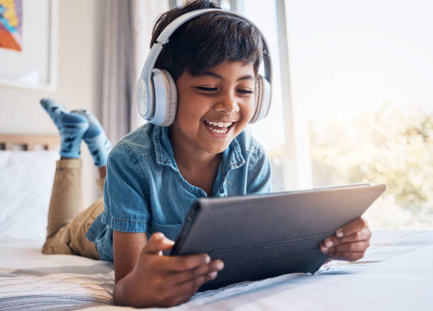 ragazzo felice, tablet e cuffie a letto, sorridi o rilassati per l'abbonamento in streaming, film o video divertenti. bambino maschio, touchscreen digitale e felice in camera da letto con tecnologia audio, spettacolo o cartone animato a casa - one little boy audio foto e immagini stock