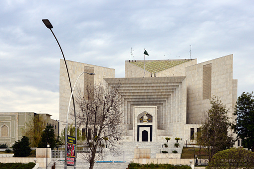 Islamabad, Pakistan: Supreme Court of Pakistan building, main entrance gate on  Constitution Avenue - Red Zone - Modernist architecture, completed in 1993, designed by the Japanese architect, Kenzo Tange, the complex was engineered and built by the CDA Engineering and Siemens Engineering - On the street a propaganda poster about Indian Occupied Kashmir.