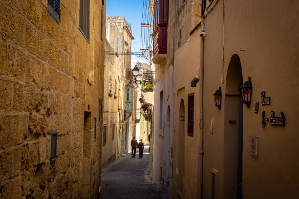 paar, das in der engen straße mit historischer architektur in der stadt rabat, gozo, malta spazieren geht. - corner stone wall brick stock-fotos und bilder