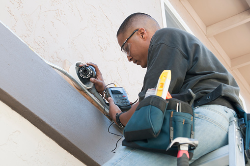 A technician uses a monitor to adjust a security camera while installing the system to the exterior of a building.