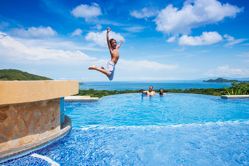 A photograph of a boy jumping into a swimming pool overlooking the Pacific.