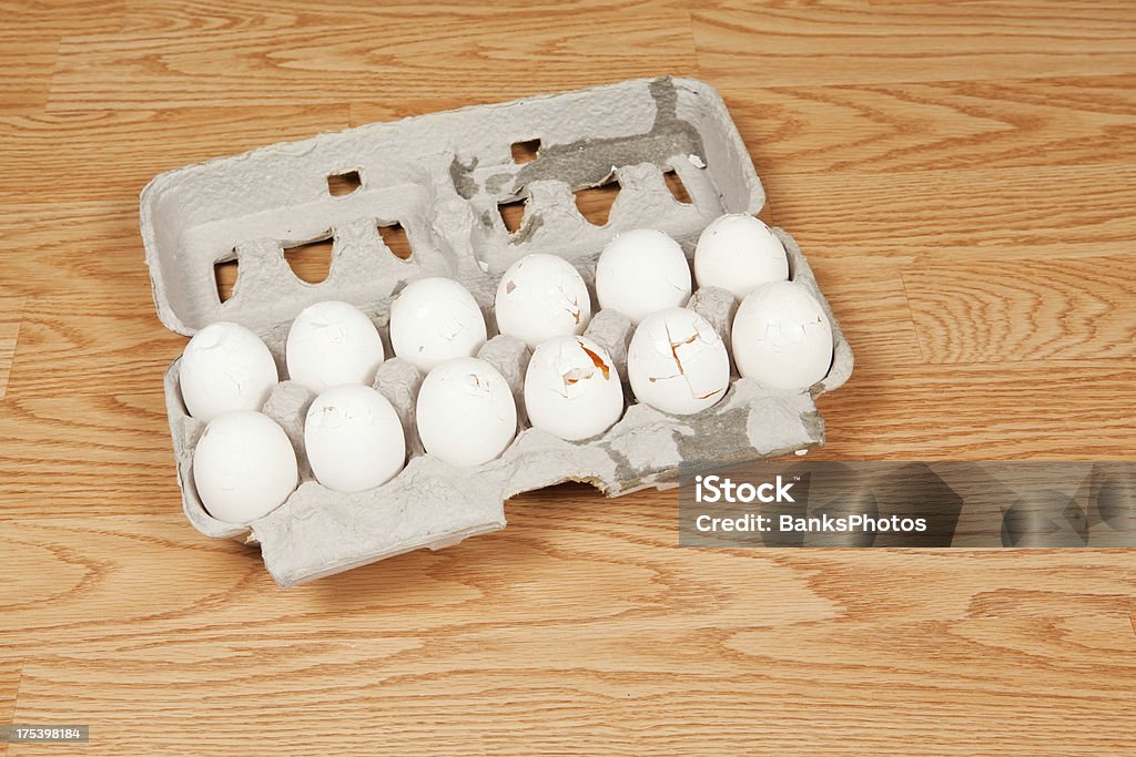 One Dozen Broken Eggs in Carton on Floor One dozen eggs have fallen to the floor and cracked. Animal Egg Stock Photo