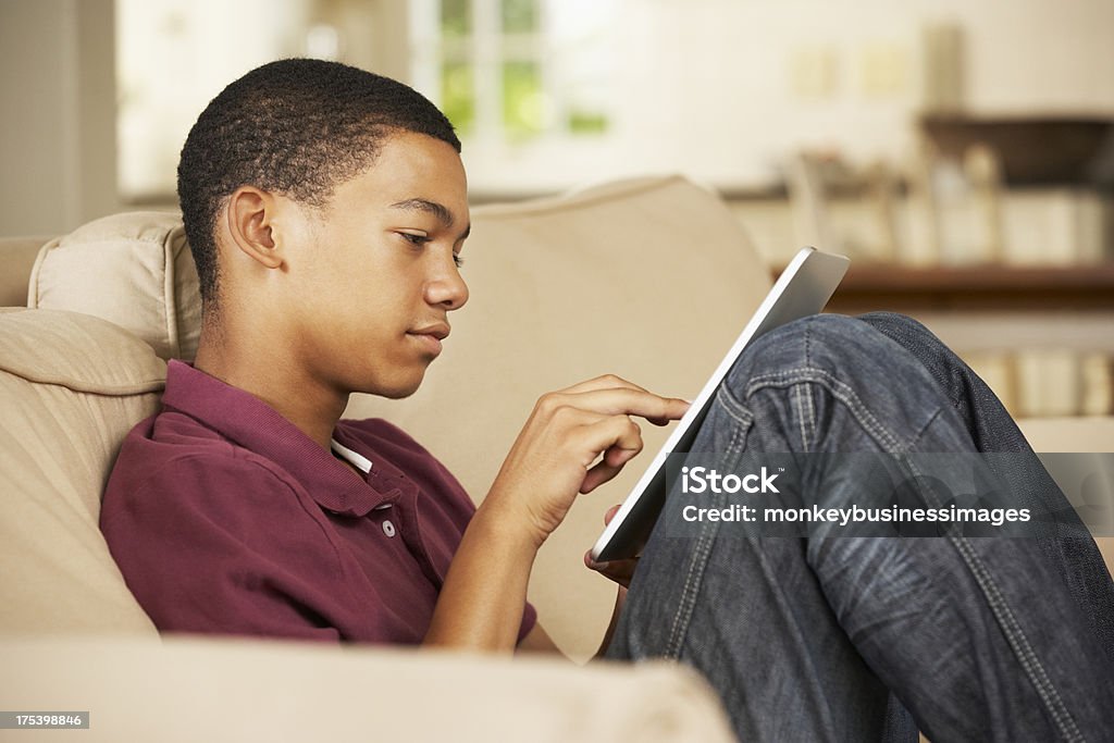 Teenage Boy Sitting On Sofa At Home Teenage Boy Sitting On Sofa At Home Using Tablet Computer Digital Tablet Stock Photo