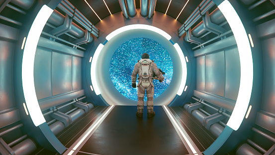 Astronaut stands inside a space ship and holds on to his helment. He looks out of a big window facing lots of stars. Concept of exploring space.
