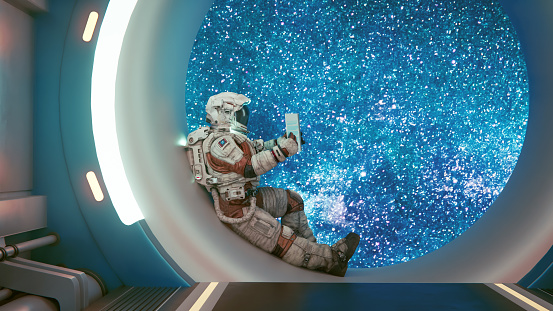 Astronaut sits in a window frame inside a space ship and reads a book about science. Concept of exploring space.