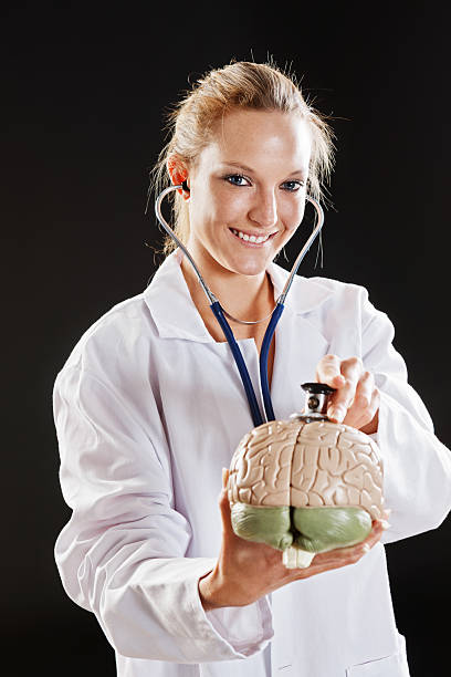 sorridente profissional médico examina loira modelo de cérebro com estetoscópio - re2012005 vertical looking at camera waist up - fotografias e filmes do acervo