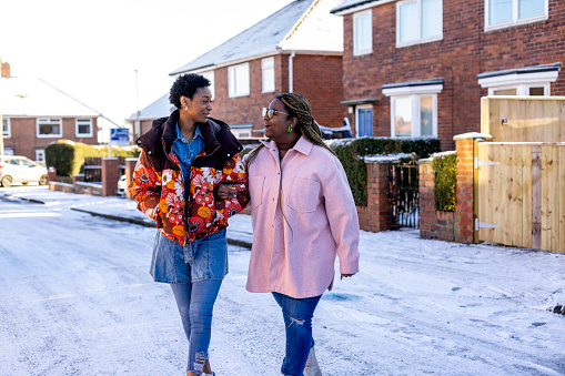 Three-quarter length shot of two young adult friends walking together through a residential street. They are walking over snow smiling and laughing together. They are located in Newcastle Upon Tyne

Video also available of this scenario.