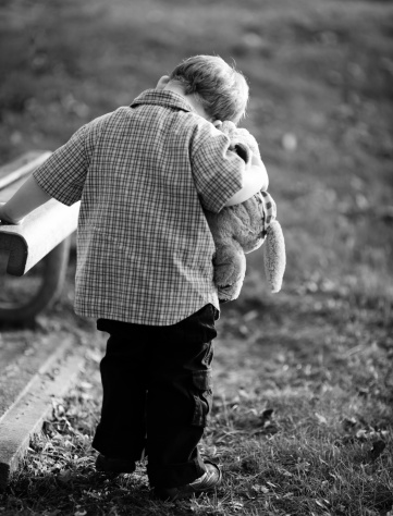 BW photo of small boy leaning down holding a teddy bear