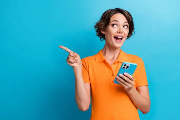 Photo of impressed funky lady wear orange t-shirt chatting apple samsung iphone showing empty space isolated blue color background.