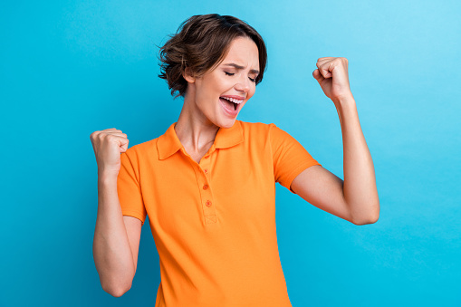 Photo of lucky funky lady wear orange t-shirt shouting yeah rising fists isolated blue color background.