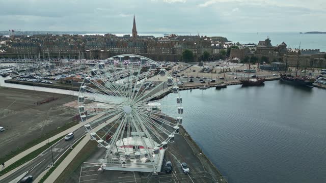 Ferris wheel with Saint-Malo port and old city in background, Brittany in France. Aerial sideways