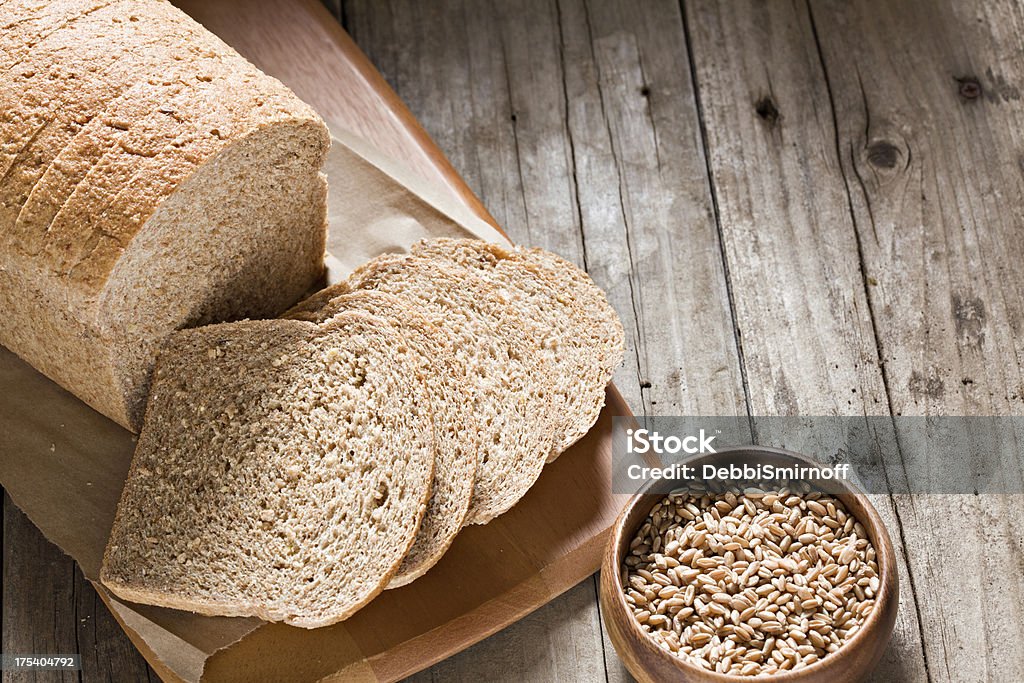 Whole Wheat Bread An overhead close up of a sliced freshly baked loaf of whole wheat bread on a cutting board laying on an old rustic picnic table and a small wooden bowl full of whet berries.Deliberate copy space on right top Bread Stock Photo