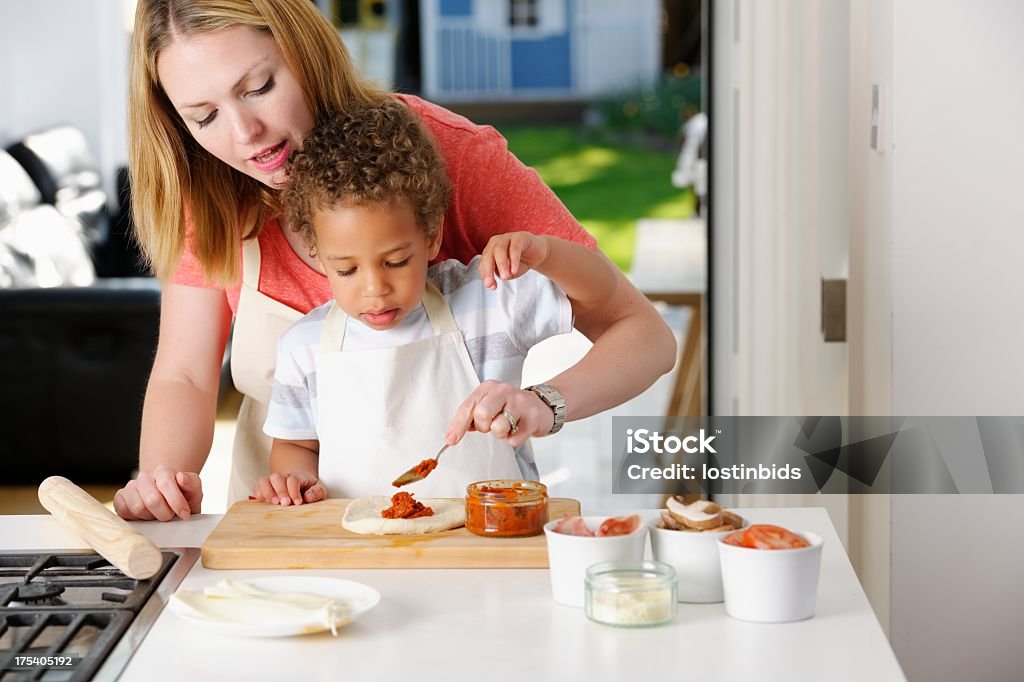 Personne de race blanche mère aider Son fils à tartiner Concentré de tomate sur la Pizza à pâte à pétrir - Photo de Pizza libre de droits