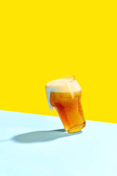 un allettante boccale di birra fredda è posizionato su uno sfondo giallo vibrante e blu pastello. - vertical studio shot indoors pink foto e immagini stock