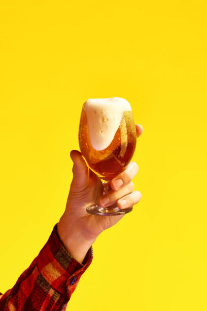 la mano maschile tiene un bicchiere di birra fredda e spumosa su sfondo giallo vibrante. - vertical studio shot indoors pink foto e immagini stock