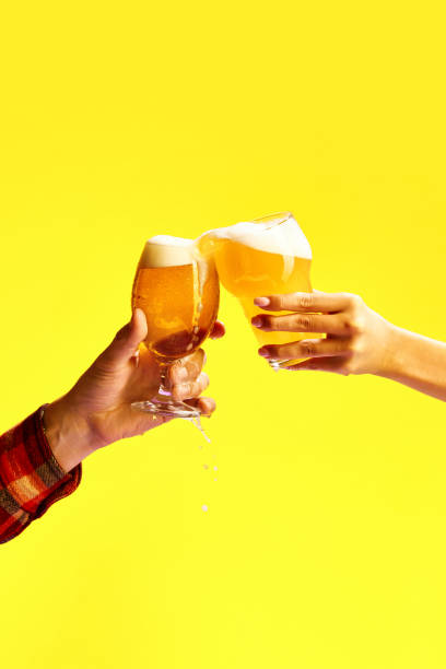 la mano maschile e femminile tiene un bicchiere di birra fredda e schiumosa su sfondo giallo vibrante. - food and drink concepts and ideas macro studio shot foto e immagini stock