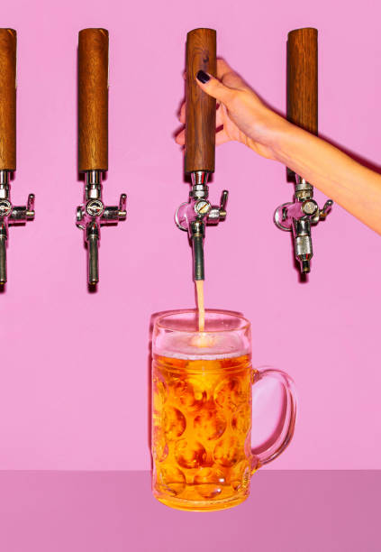 mano femminile che versa birra leggera dal rubinetto in un bicchiere refrigerato. la birra si forma densa, schiumosa mentre scende a cascata nel boccale. - vertical studio shot indoors pink foto e immagini stock