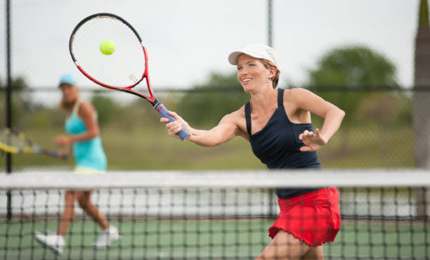 mujer joven jugando al tenis con camas dobles - tennis women action lifestyles fotografías e imágenes de stock