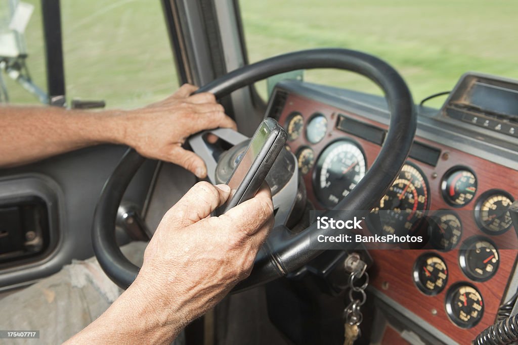 Truck Driver Using Mobile Phone "An over-the-road semi truck driver is using a mobile phone while driving which is illegal in many areas. The truck is a late 1990s model, the drivers hands are worn from work, jeans ripped and the phone and dash have some visible dust/wear. This would make a good construction (dump truck) or agricultural transportation image." Driving Stock Photo