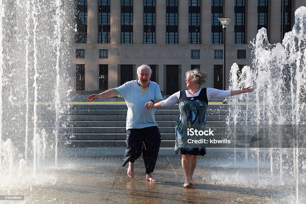 mature couple dance in fountains a mature / senior couple hold hands and dance in celebration in some sunlit fountains Fountain Stock Photo