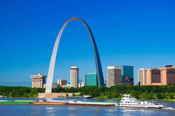 St. Louis skyline, arch, river, and boat "Downtown St. Louis skyline with the Gateway Arch, the Jefferson National Expansion Memorial park, the Mississippi River, and a cargo barge." jefferson national expansion memorial park stock pictures, royalty-free photos & images