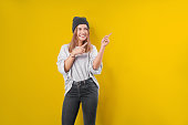 Young woman in a sweatshirt on a yellow studio background, excited pointing with forefingers away.