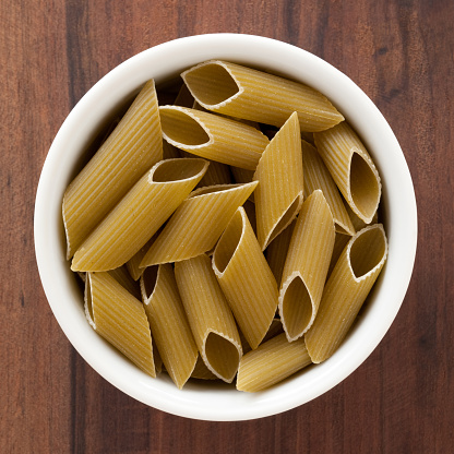 Top view of white bowl full of penne dried pasta