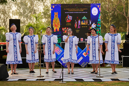 New Delhi, India - 10.12.2022 - Outdoor public park. Female choir musical ensemble of russian folk songs perform vocal music at indian charity christmas fair, group of woman singing russian folk song at outdoor stage