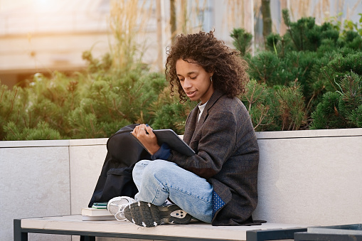 Young african american woman sitting on a bench and using tablet. People, friendship, studying, lifestyle concept