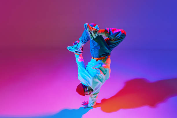 Man in stylish sportswear in motion, dancing breakdance isolated over gradient studio background in neon light