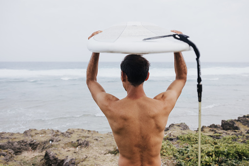 A determined surfer marching towards the waves, surfboard balanced on his head