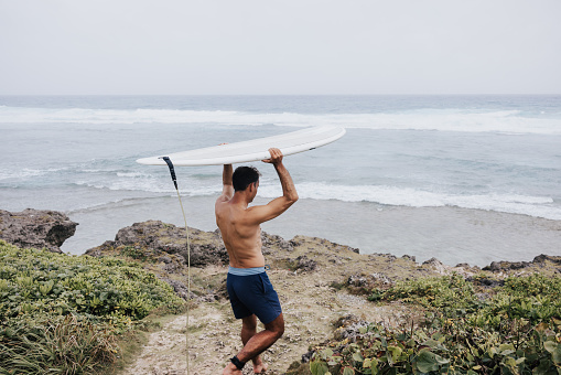A beach scene with a lone surfer in board shorts, heading towards the water with his surfboard under his arm.