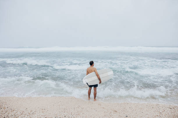 The surfer stands in the refreshing water, his surfboard ready for the next adventure.