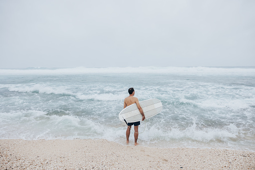 The surfer stands in the refreshing water, his surfboard ready for the next adventure.